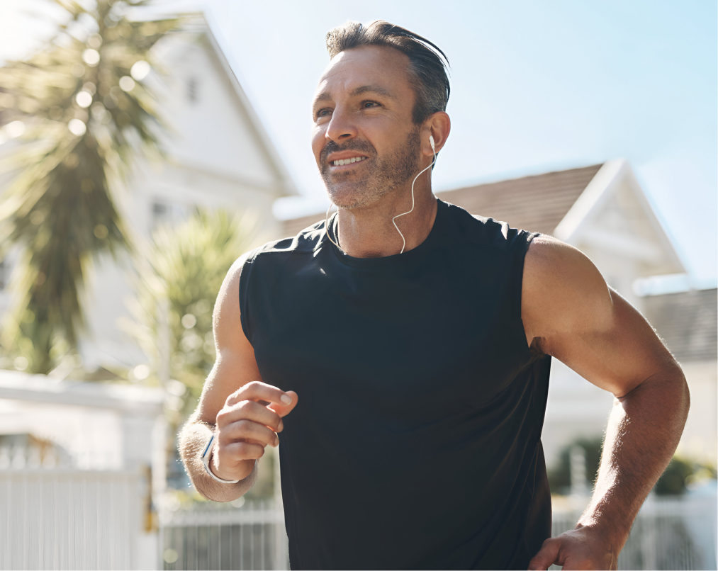 Man jogging outdoors in suburban neighborhood wearing earbuds and black sleeveless shirt