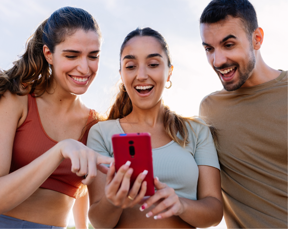 Three smiling people looking at a red phone together outdoors