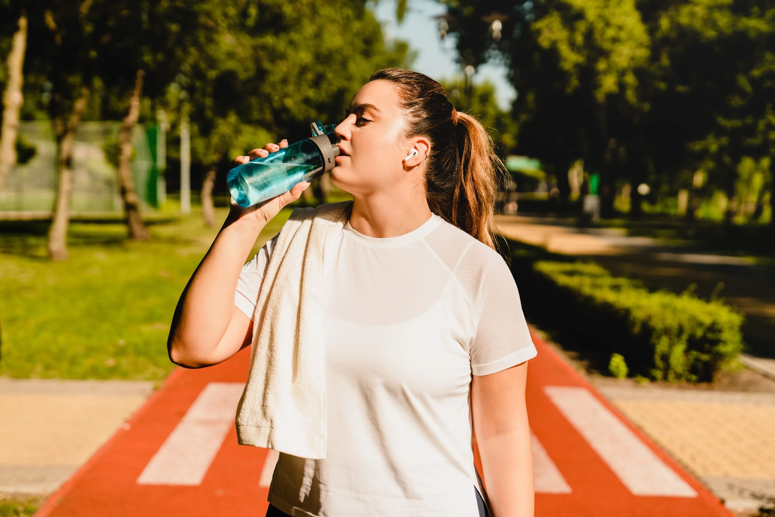 Athletic woman drinking water outdoors on a park path