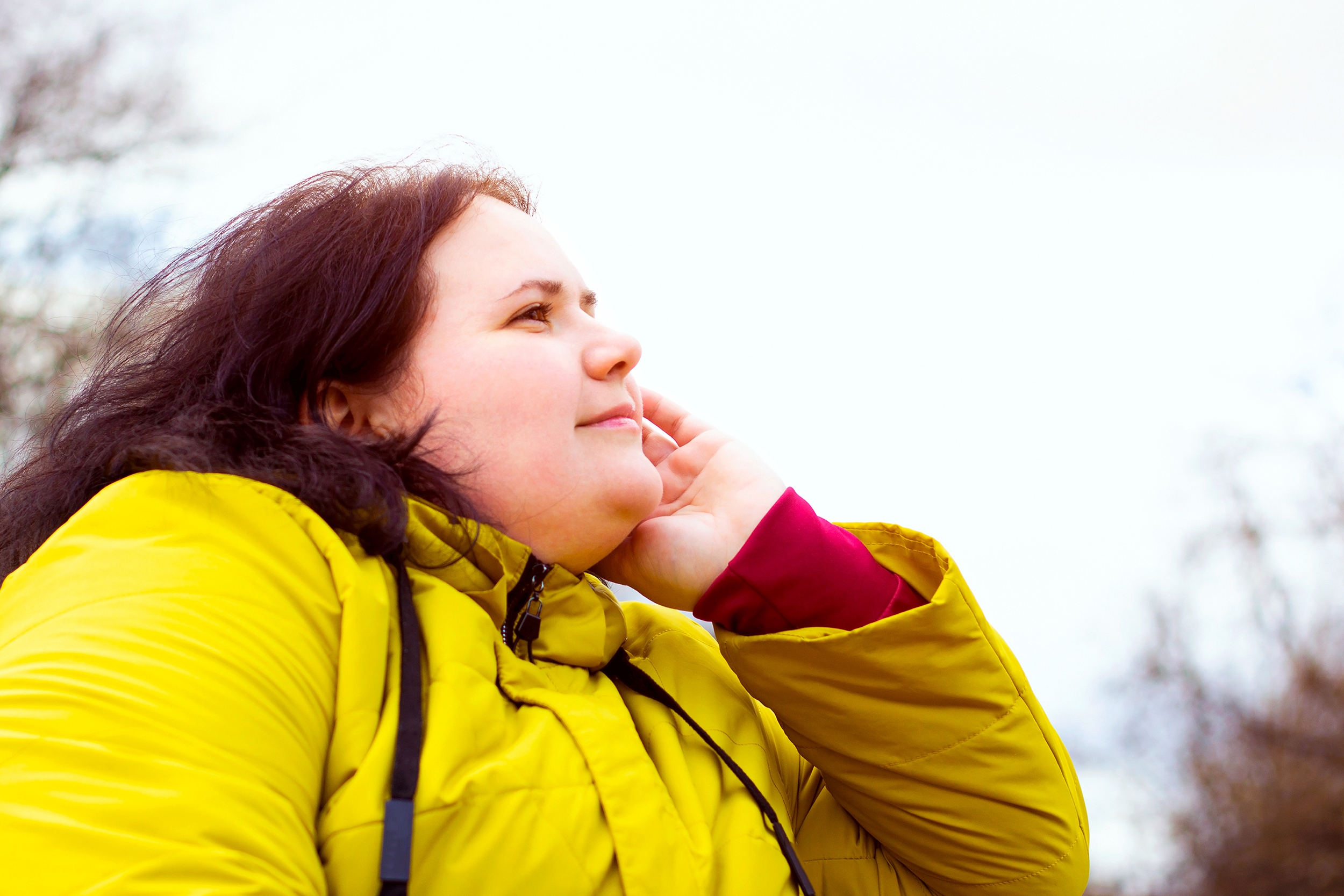 Woman in yellow jacket looking thoughtfully outdoors