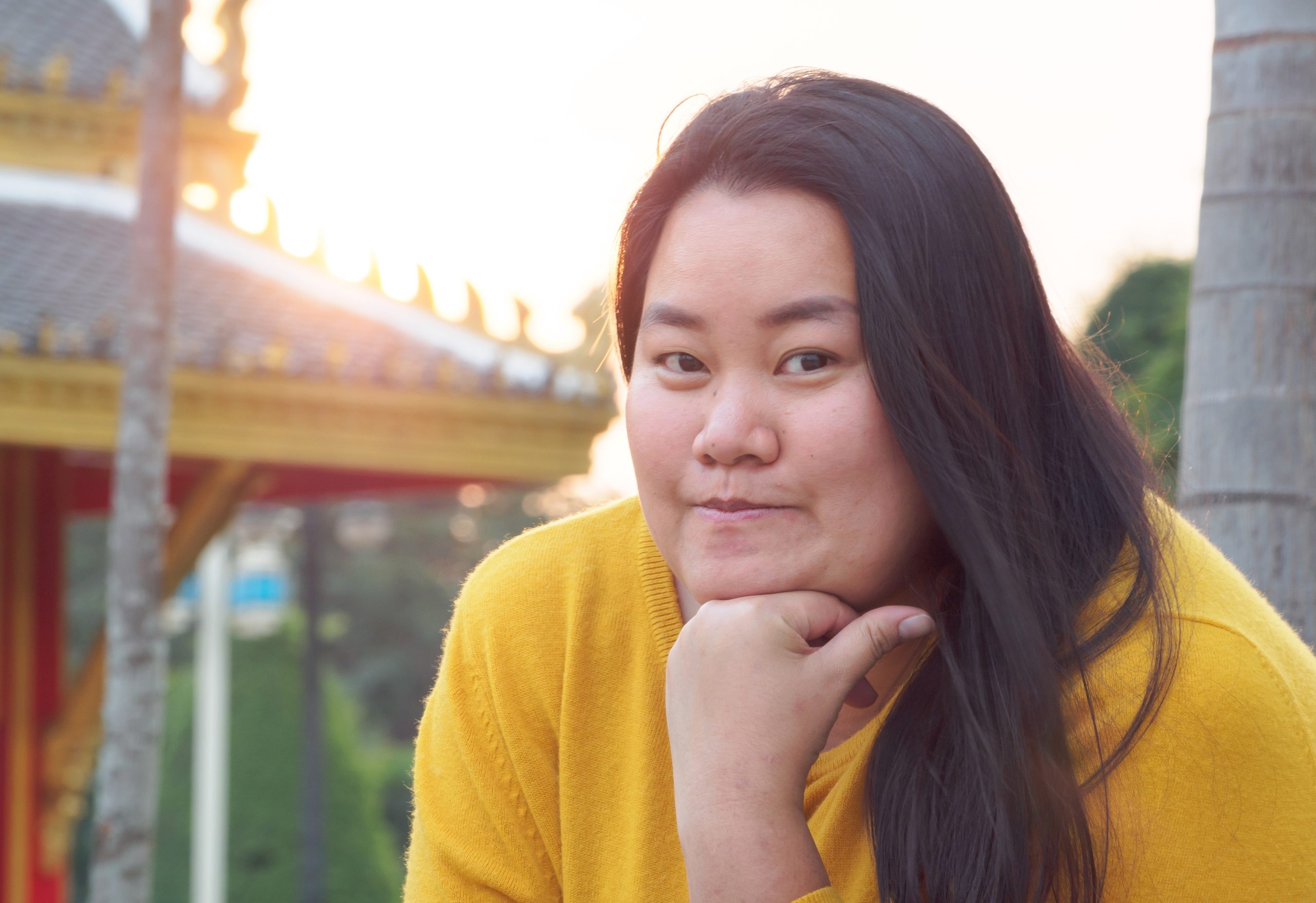 Woman in yellow jacket posing outdoors with hand on chin