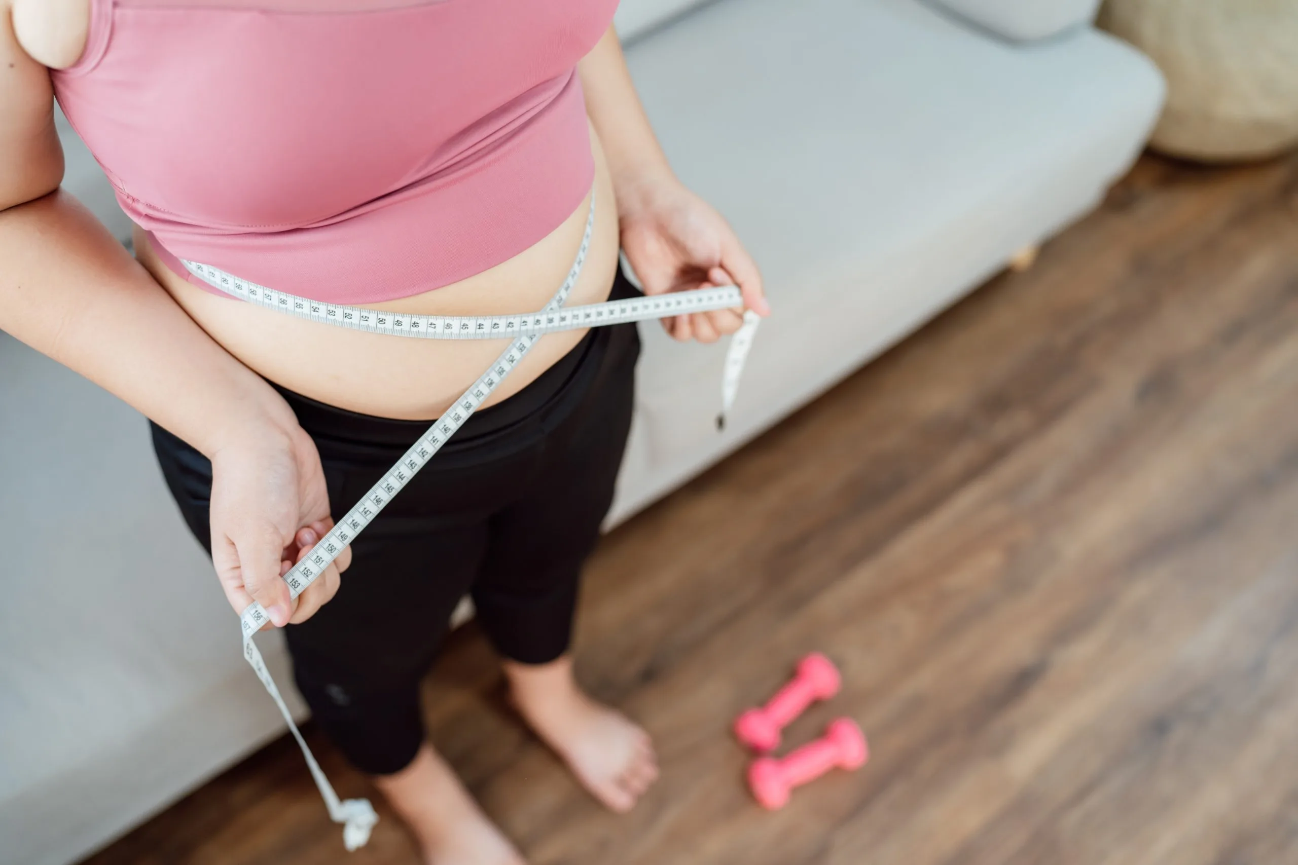 Woman measuring her waist with a tape measure during weight loss progress tracking