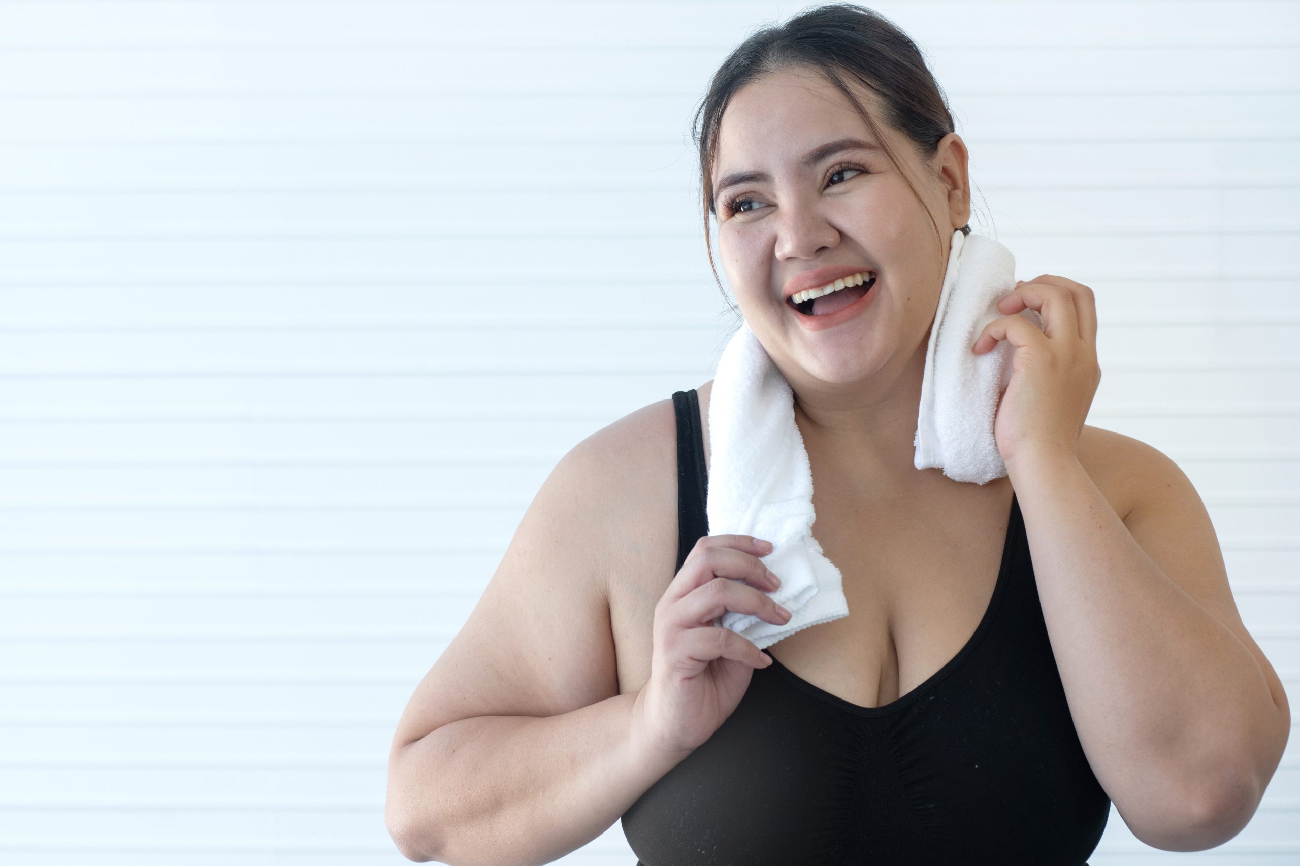 Woman in athletic wear wiping sweat from her face with a white towel after exercise
