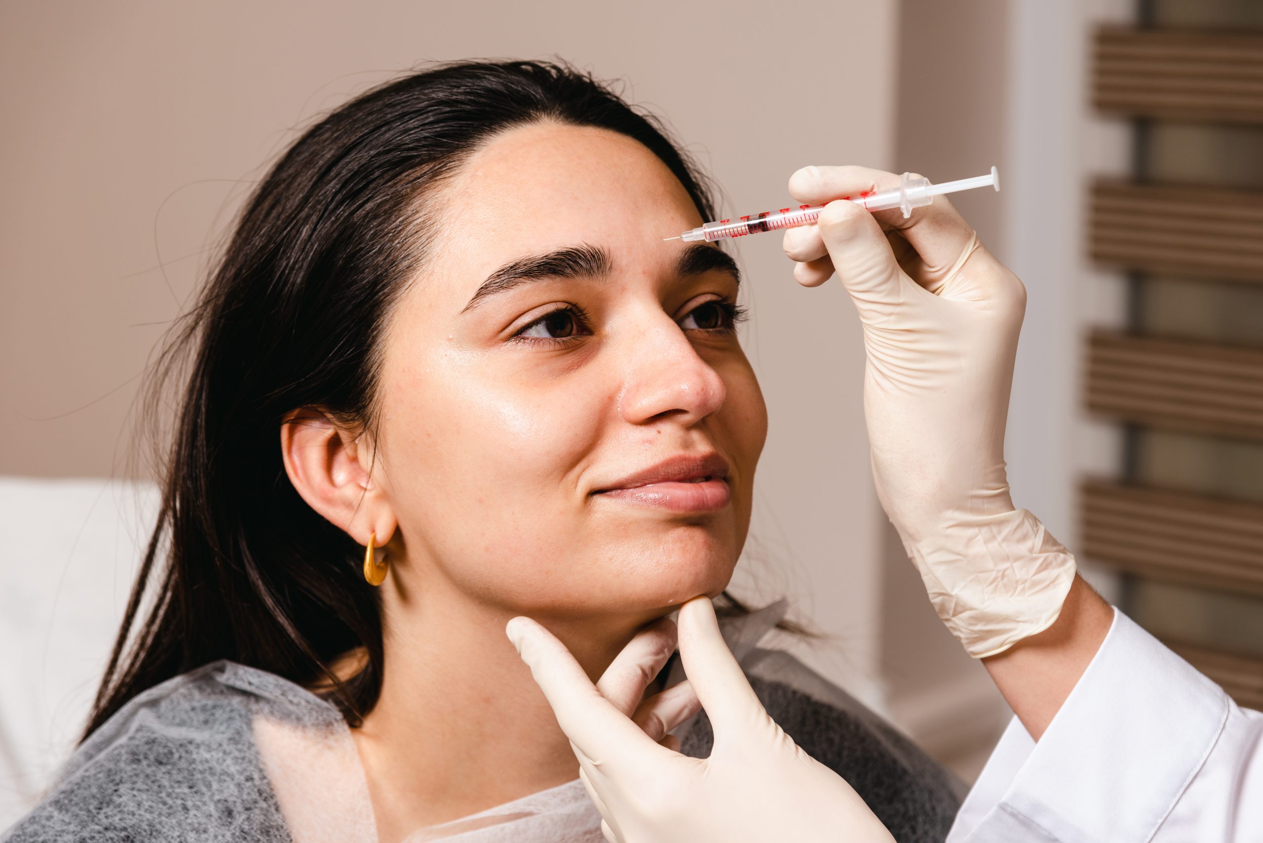Doctor injecting filler along woman's temple area during aesthetic treatment