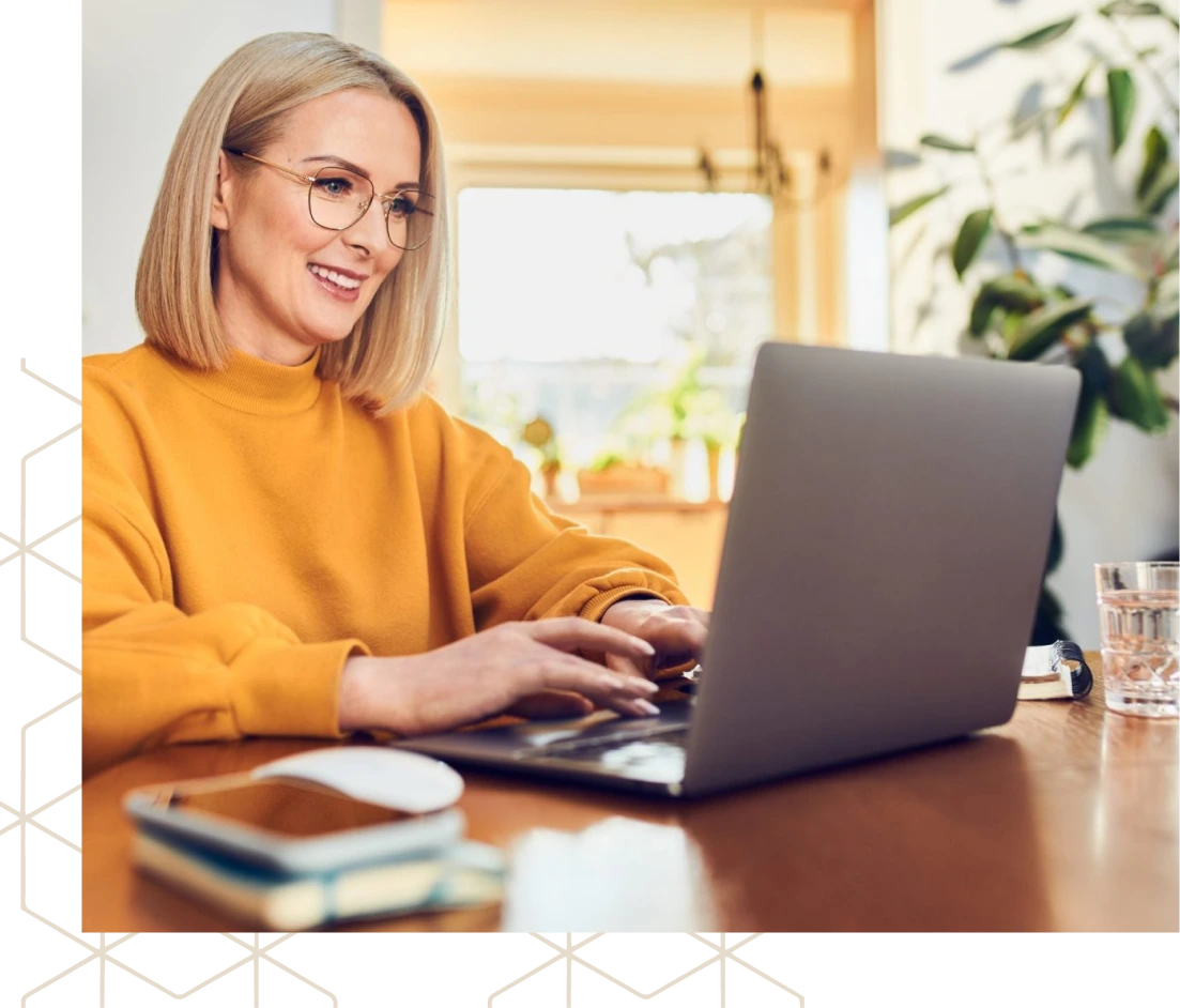 Woman in yellow shirt smiling while typing on laptop at desk