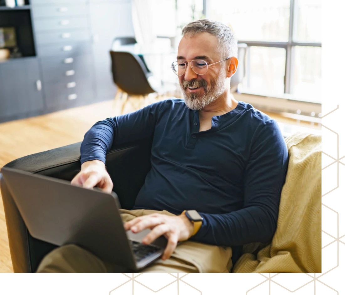 Man wearing glasses smiling while using laptop at desk in modern office