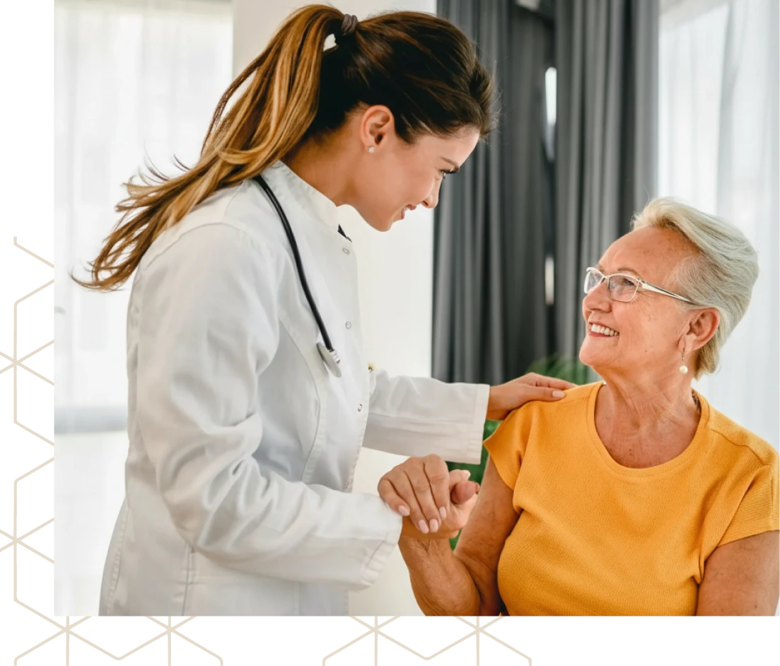 Healthcare provider in white coat with stethoscope speaking with older patient in yellow shirt