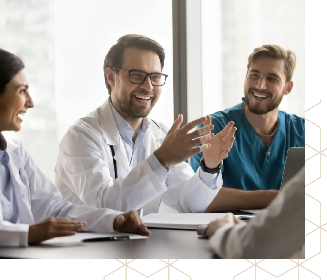 Healthcare team members in white coats and scrubs collaborating at laptop during meeting