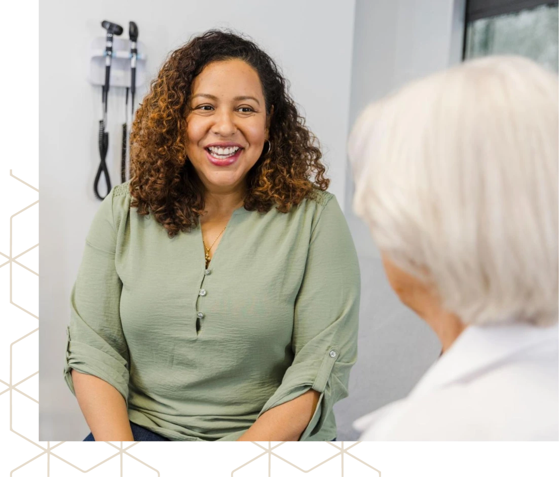 Smiling clinician in green shirt speaking with senior patient in treatment room