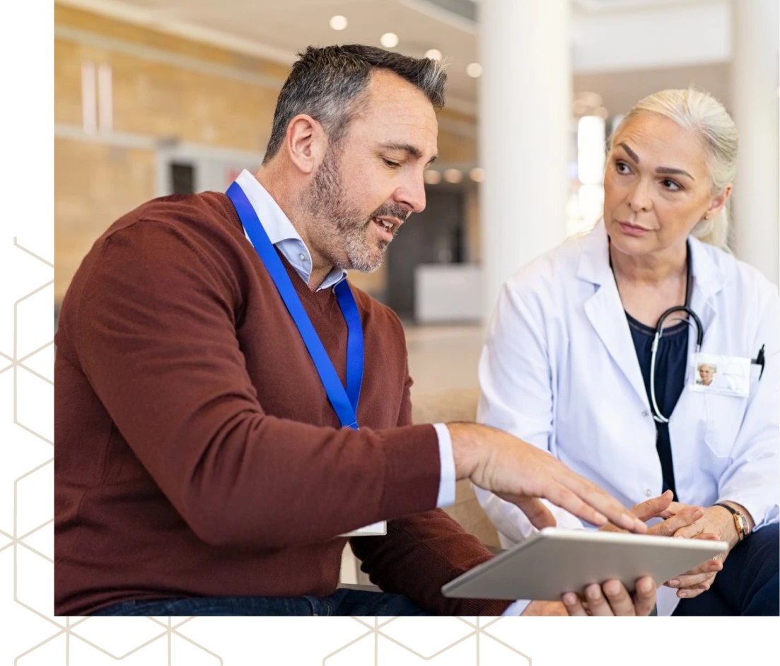 Man wearing ID badge reviewing tablet with female healthcare provider in hospital corridor