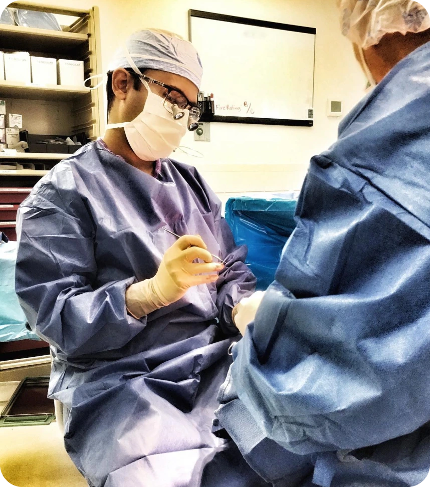 Surgeon in blue scrubs and surgical mask with magnifying loupes examines patient during oculofacial procedure