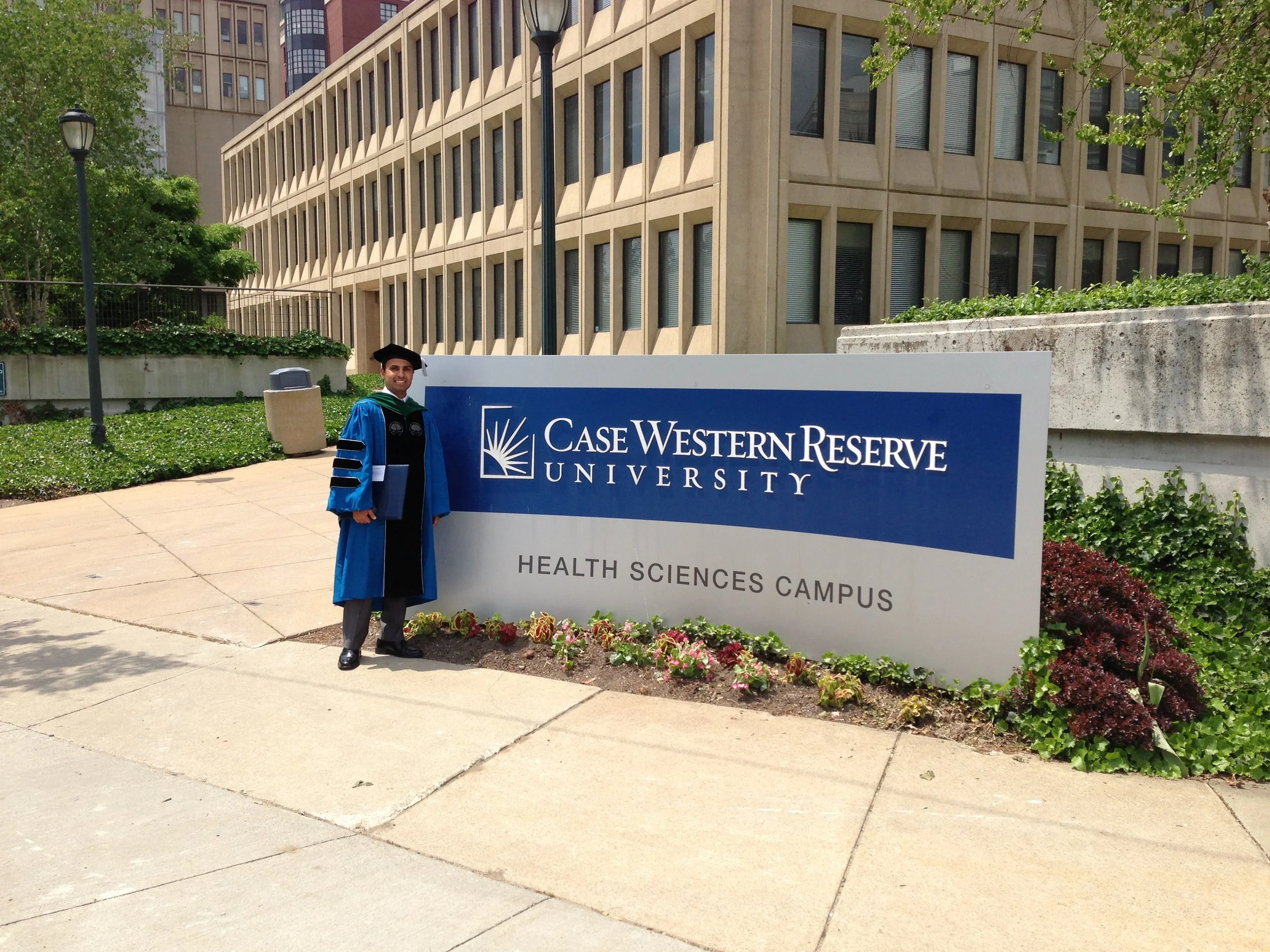Graduate in blue and black regalia standing beside Case Western Reserve University Health Sciences Campus sign