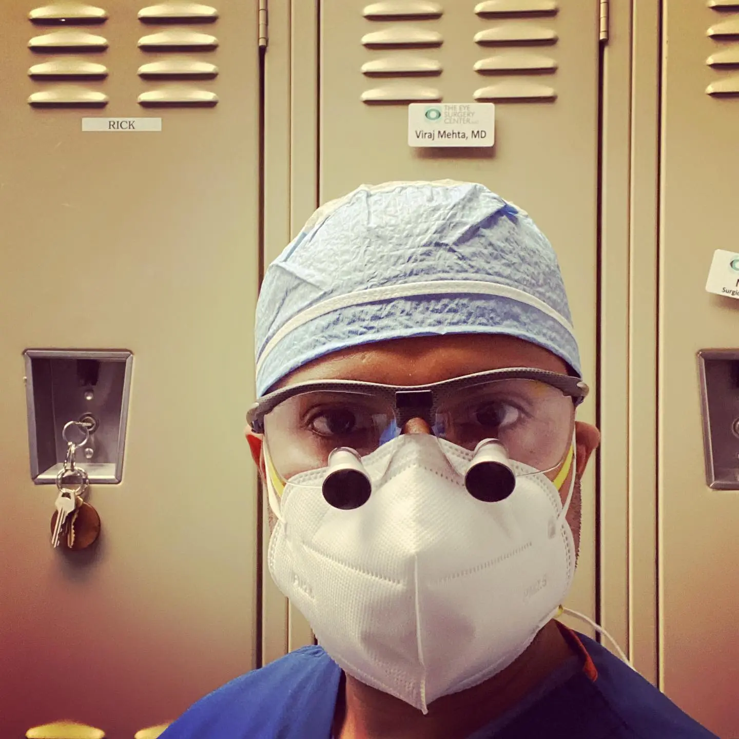 Viraj Mehta, MD in surgical headwrap and protective eyewear with name placard on locker background