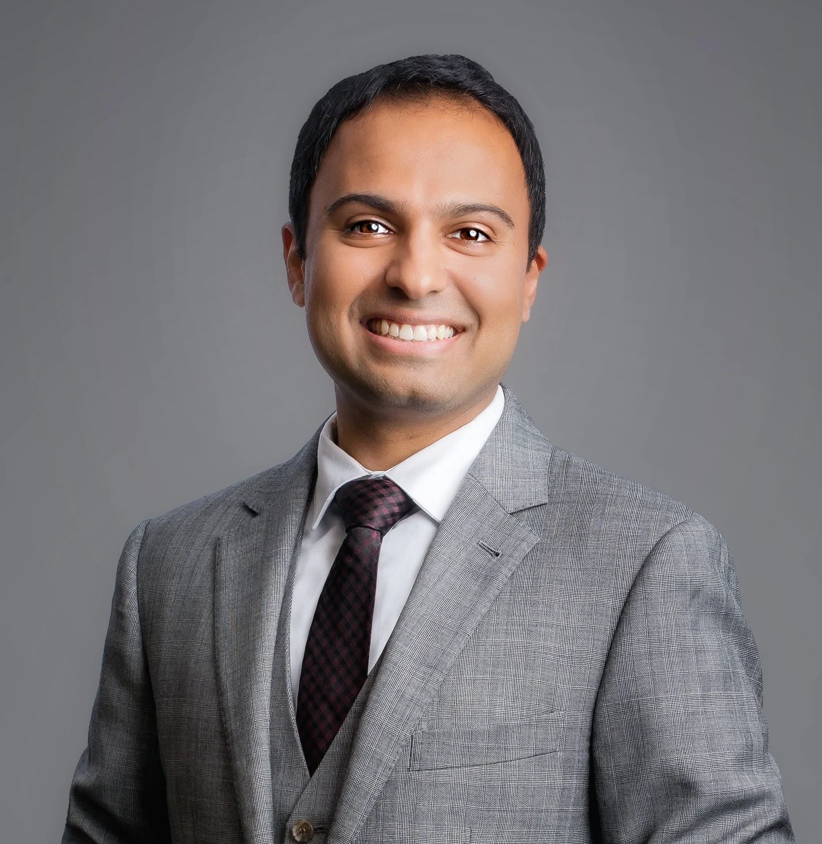 Man in gray suit and purple tie smiling at camera against gray background