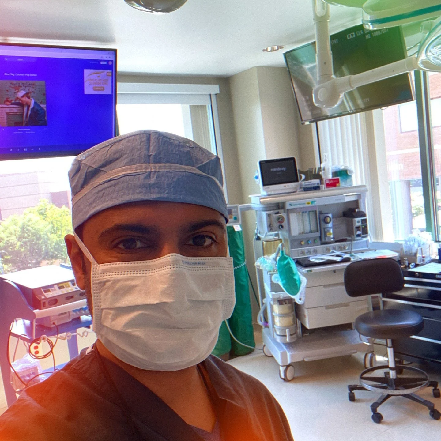 Surgeon in surgical mask and cap inside operating room with surgical equipment and blue monitor display