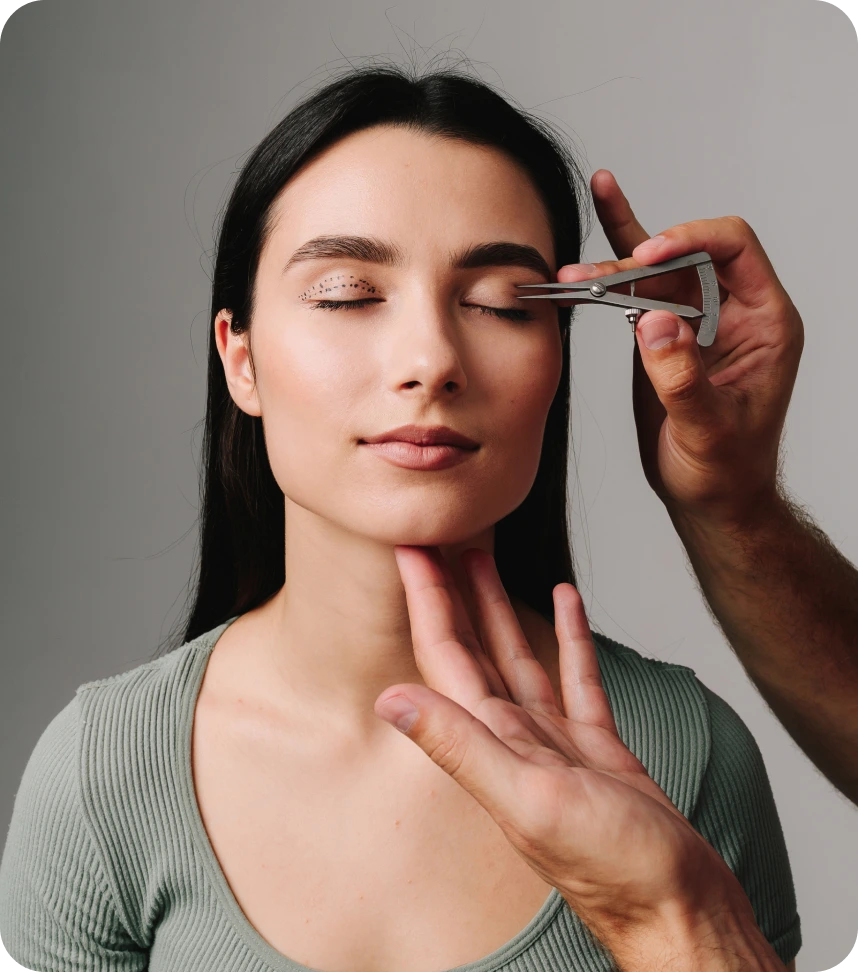 Clinician using calipers to measure eyelid area on patient's face during consultation