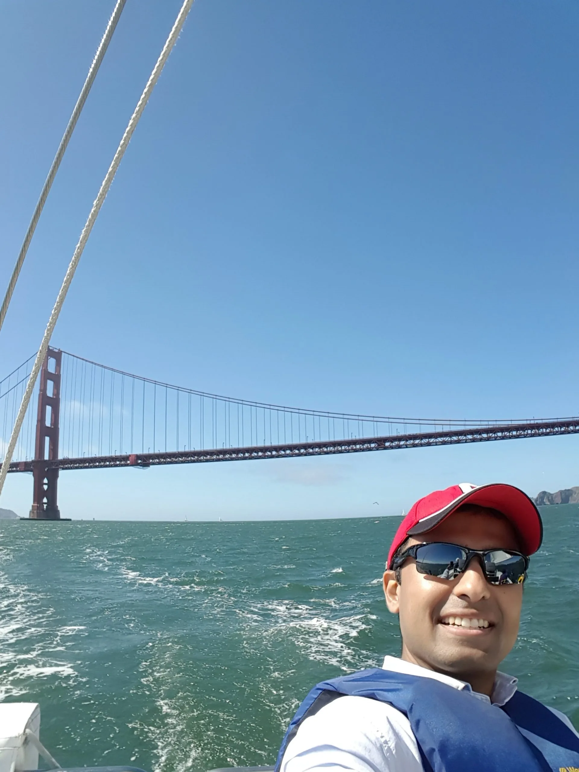 Man in red cap and sunglasses on boat with Golden Gate Bridge in background