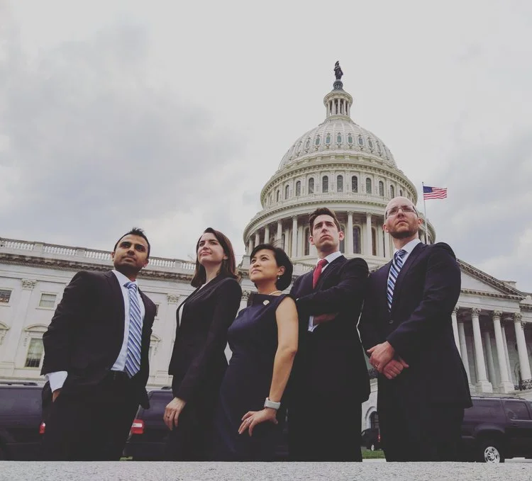 Five professionals in business attire standing in front of the U.S. Capitol building