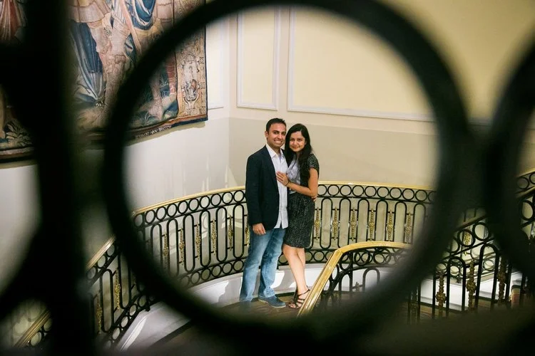 Couple standing together on ornate staircase viewed through decorative railing