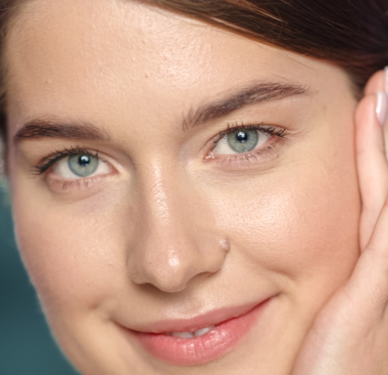 Woman with green eyes touching her face, showing clear complexion and smile