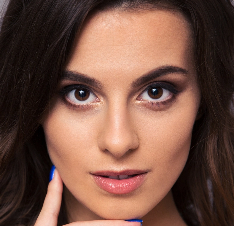 Woman with dark hair looking directly at camera, showing clear skin and defined eyebrows