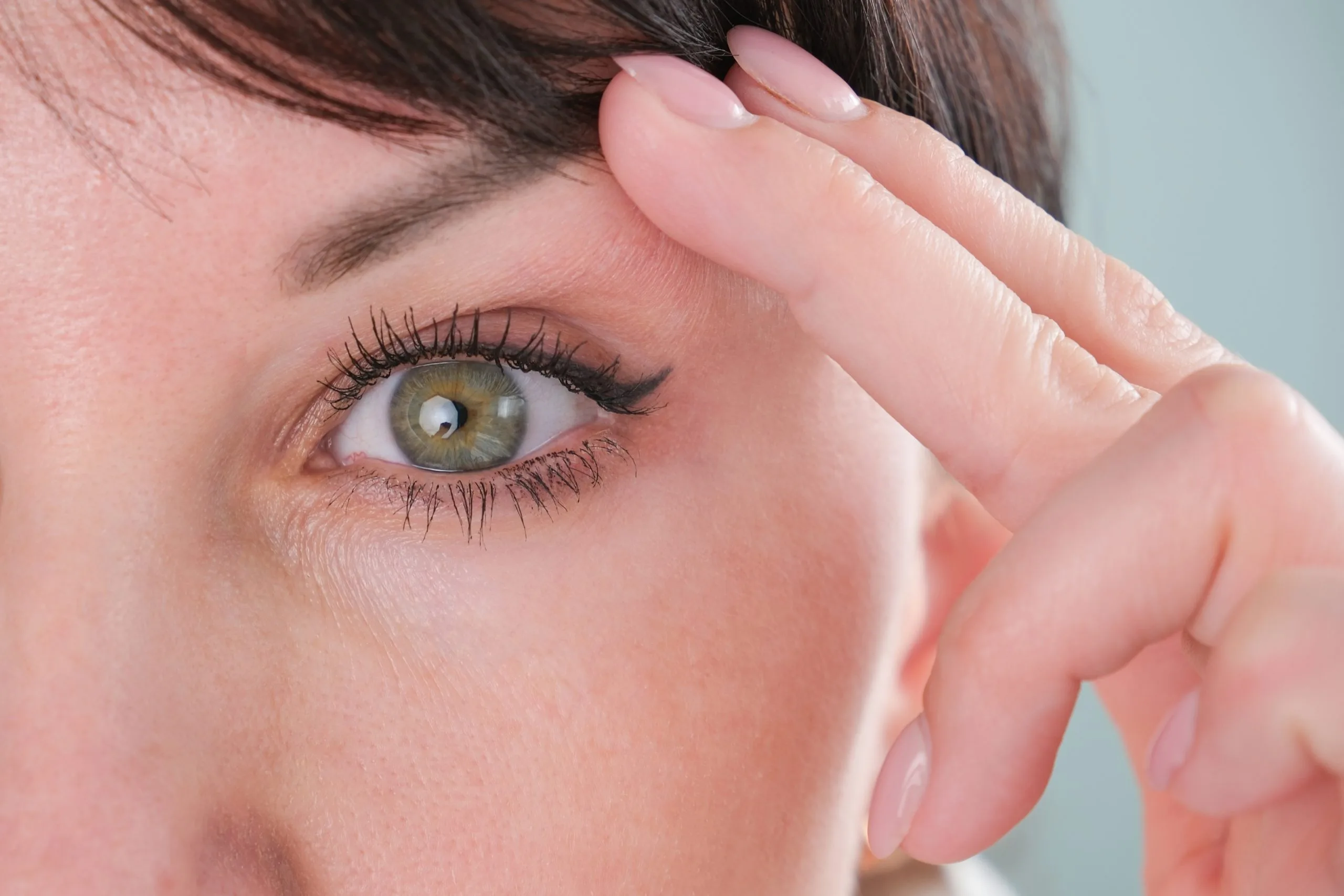 Woman's face in profile with hand pulling upper eyelid to show eye anatomy
