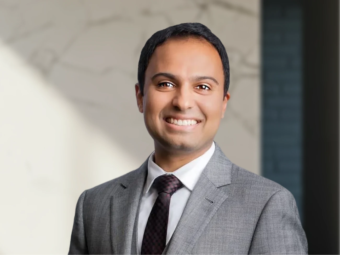 Surgeon in gray suit and burgundy tie smiling at camera in professional portrait