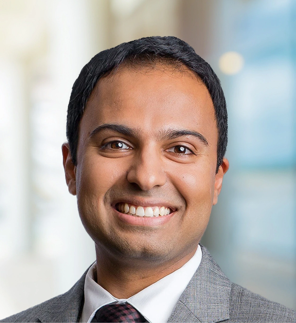 Man in gray suit and burgundy tie smiling at camera with blurred background
