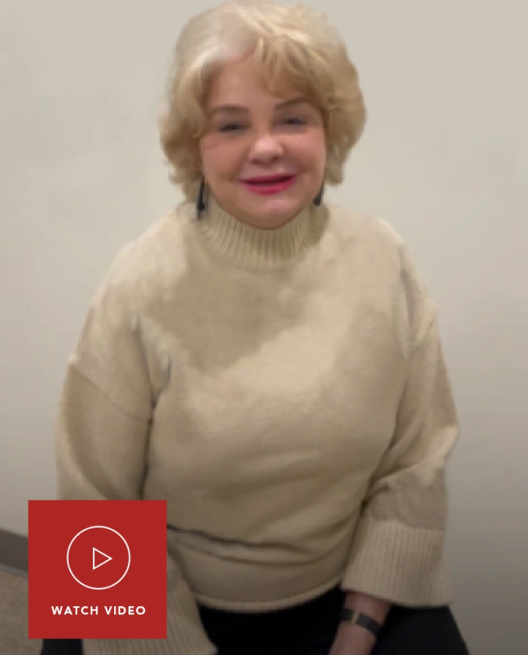 Woman with short blonde hair wearing cream turtleneck with play button and WATCH VIDEO text overlay