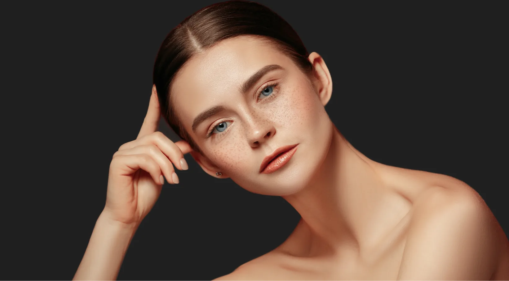 Woman with clear skin touching her face against dark background