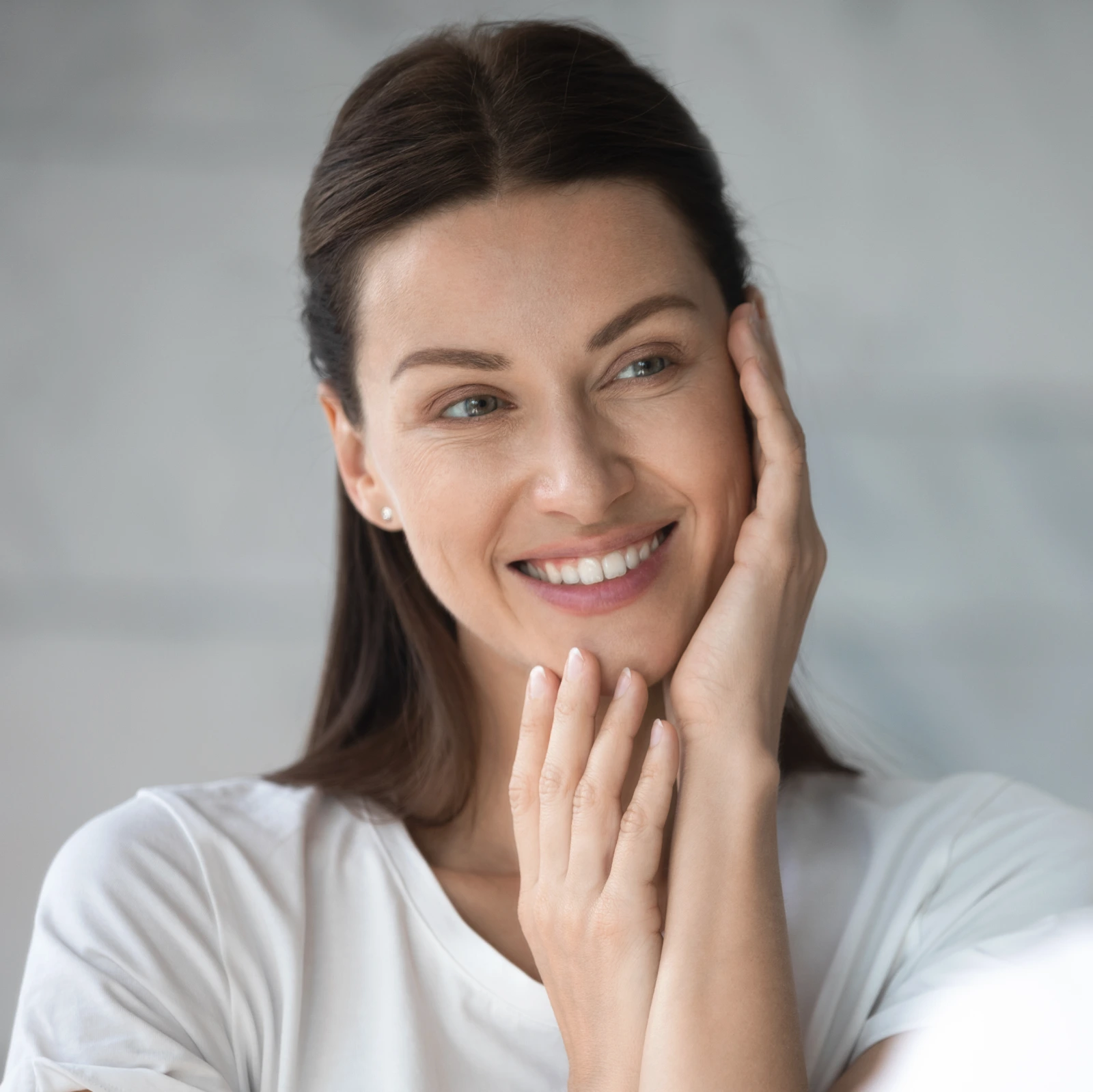 Smiling woman in her thirties touching her glowing, hydrated skin
