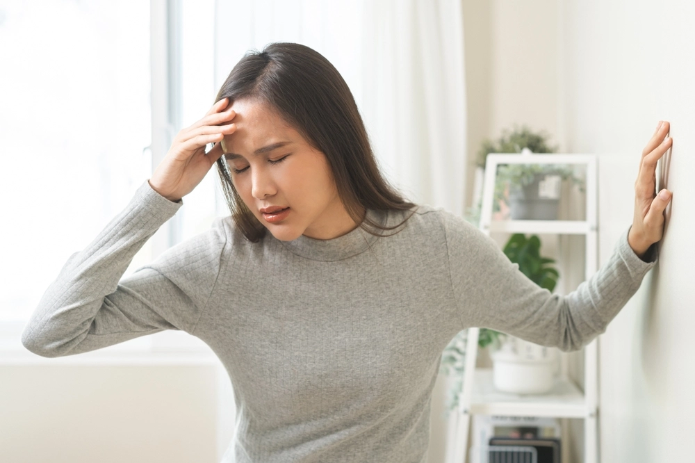 Woman holding her head with hand, experiencing a headache indoors