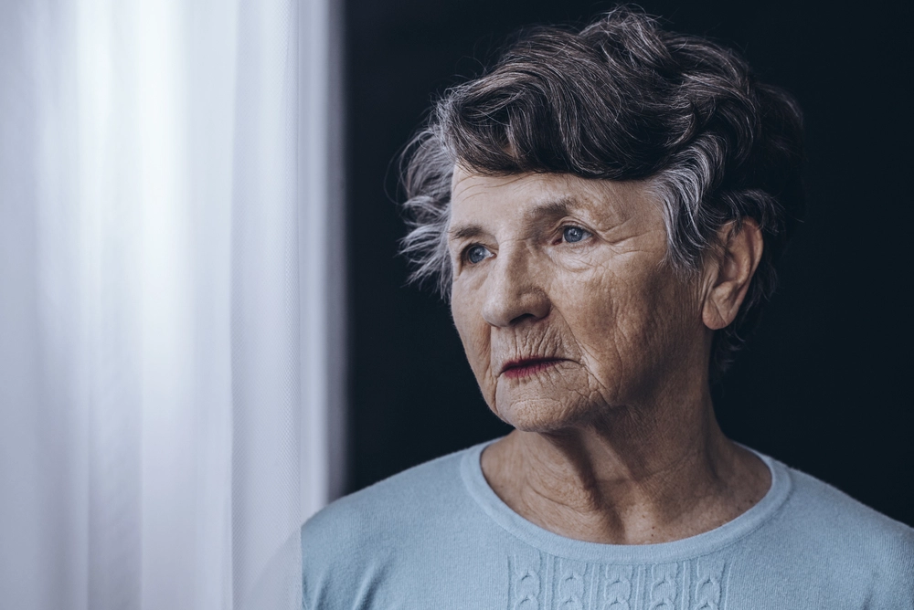 Older woman with gray hair looking pensively to the side in a light blue shirt