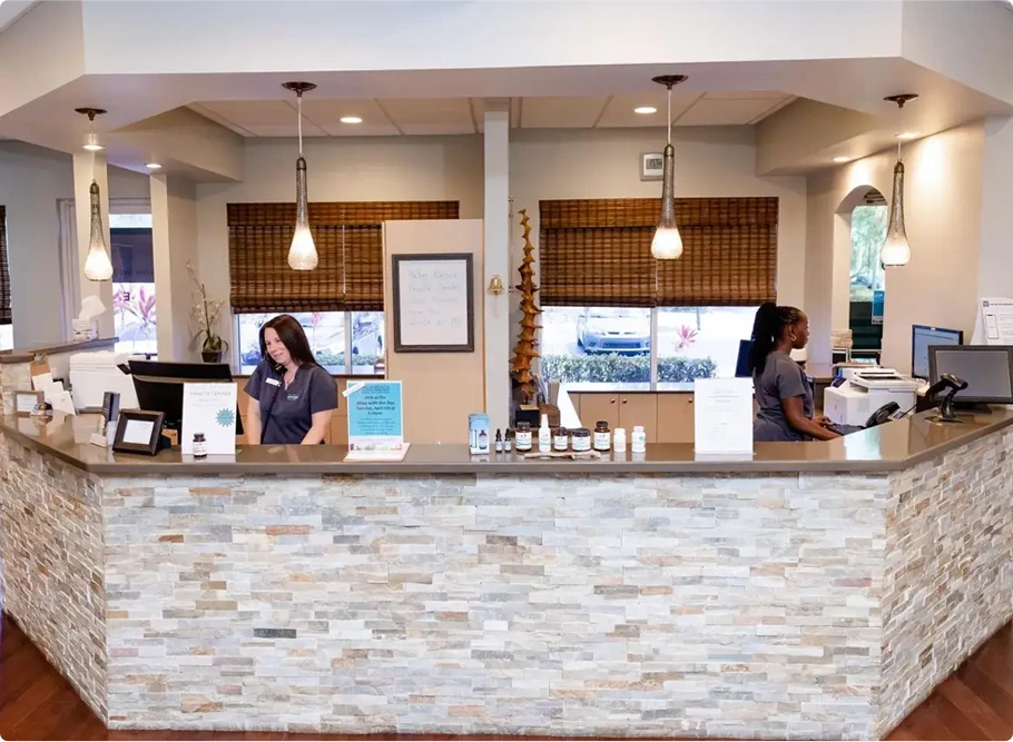 Palm Beach Health Center reception desk with two staff members behind a curved stone counter and pendant lighting