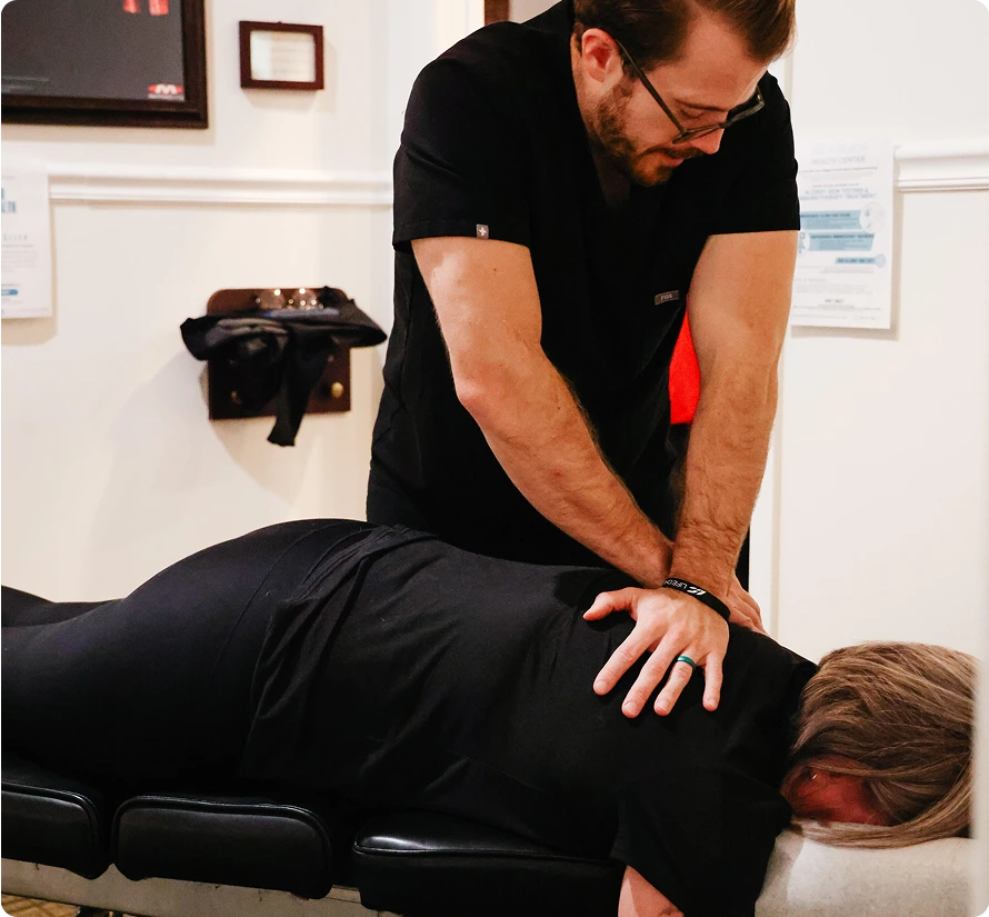 Chiropractor performing spinal manipulation on a patient lying face-down on treatment table