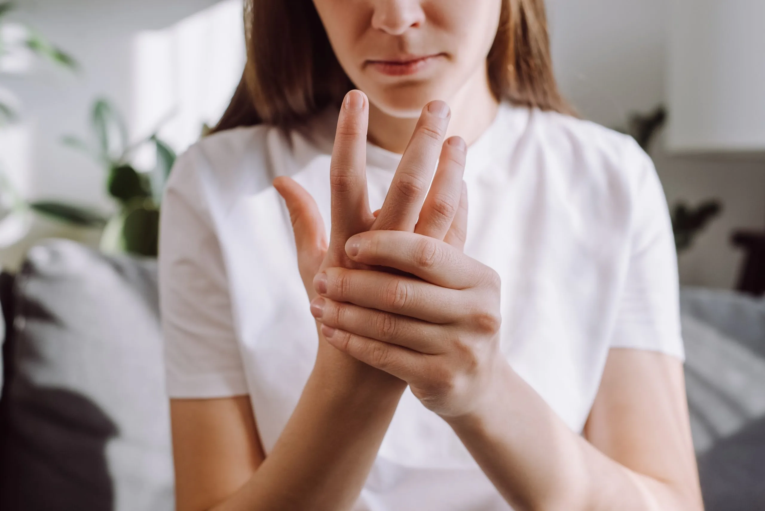 Woman in white shirt holding her hand with visible discomfort in her palm
