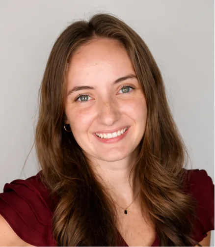Woman with long brown hair smiling at camera wearing maroon top