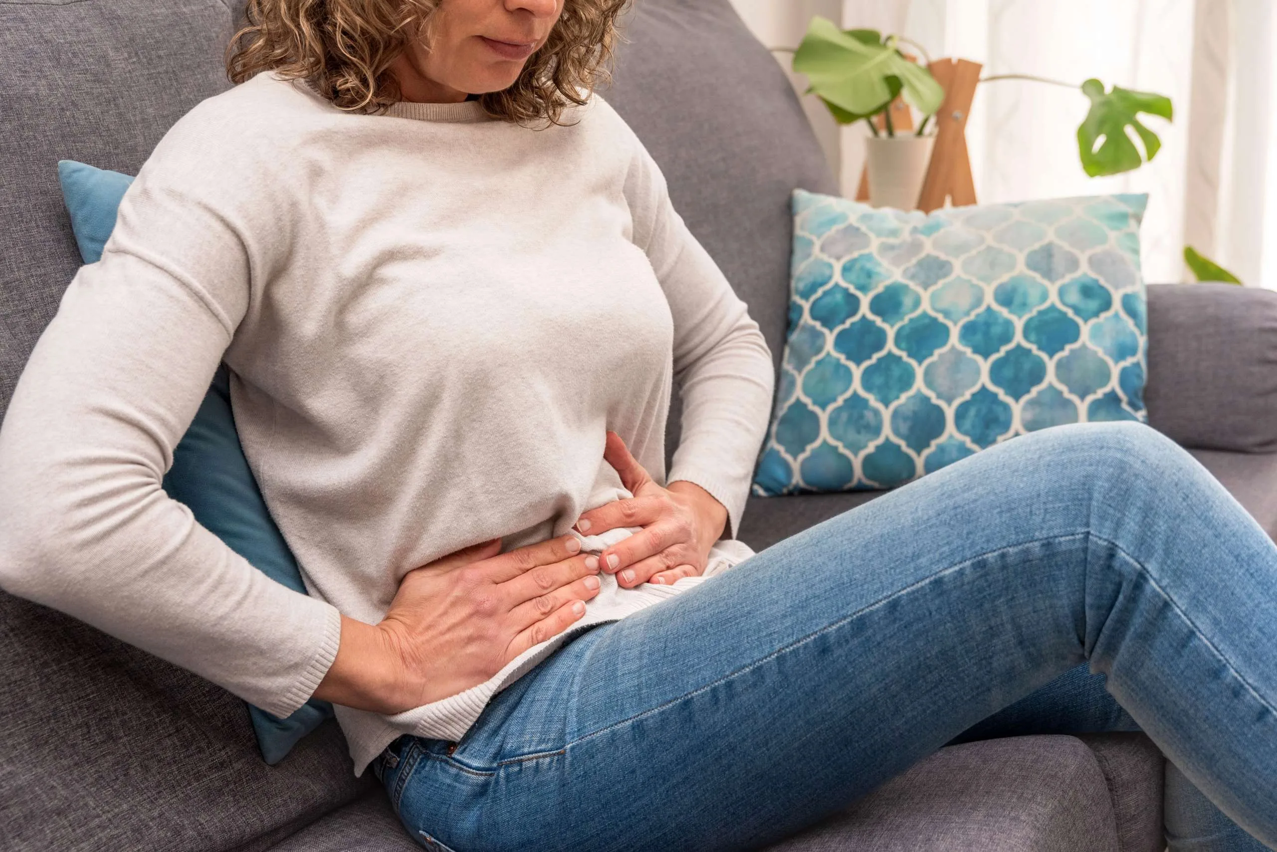Woman on sofa holding her abdomen, experiencing digestive discomfort