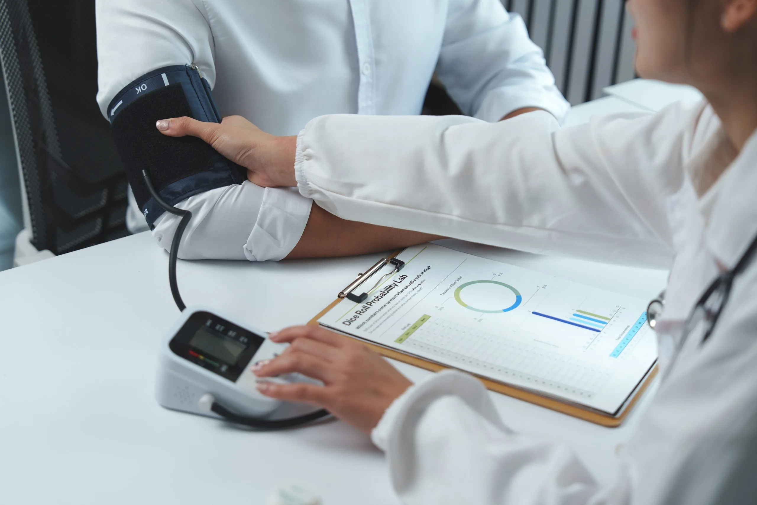 Healthcare provider checking patient's blood pressure while reviewing health chart