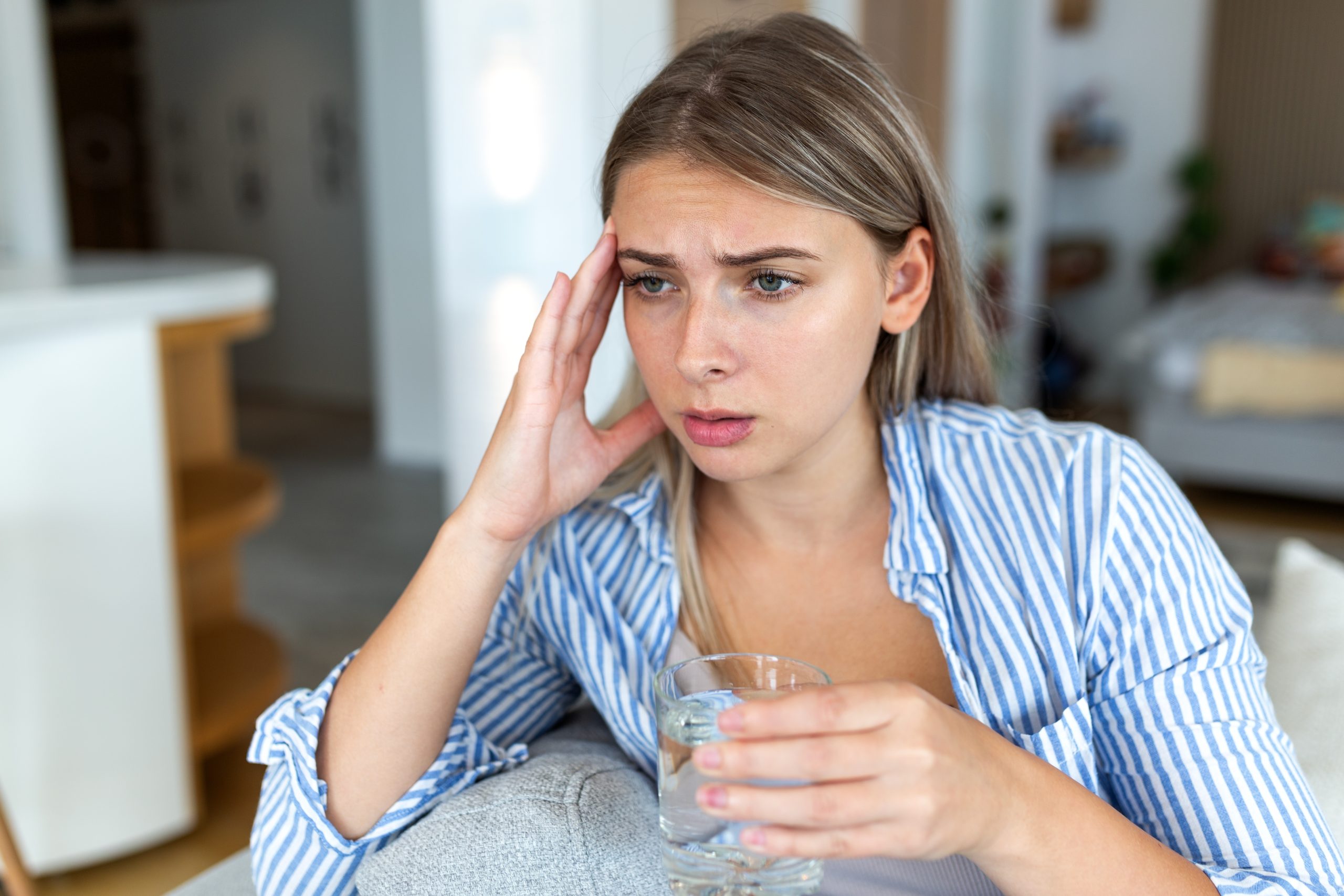 Woman holding water glass looking concerned about headache or illness at home
