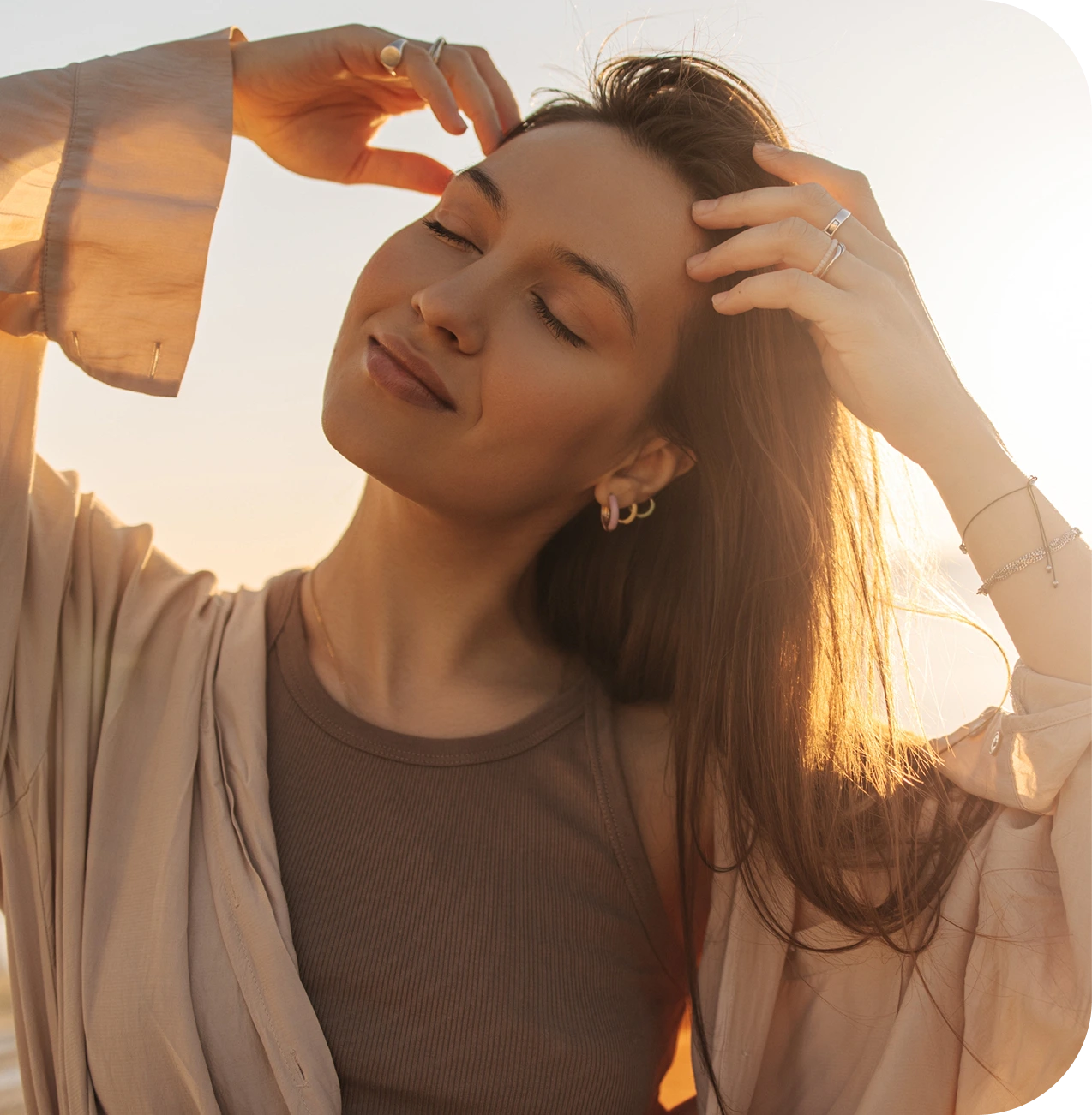 Woman in sunlight holding her hair back with eyes closed, smiling peacefully