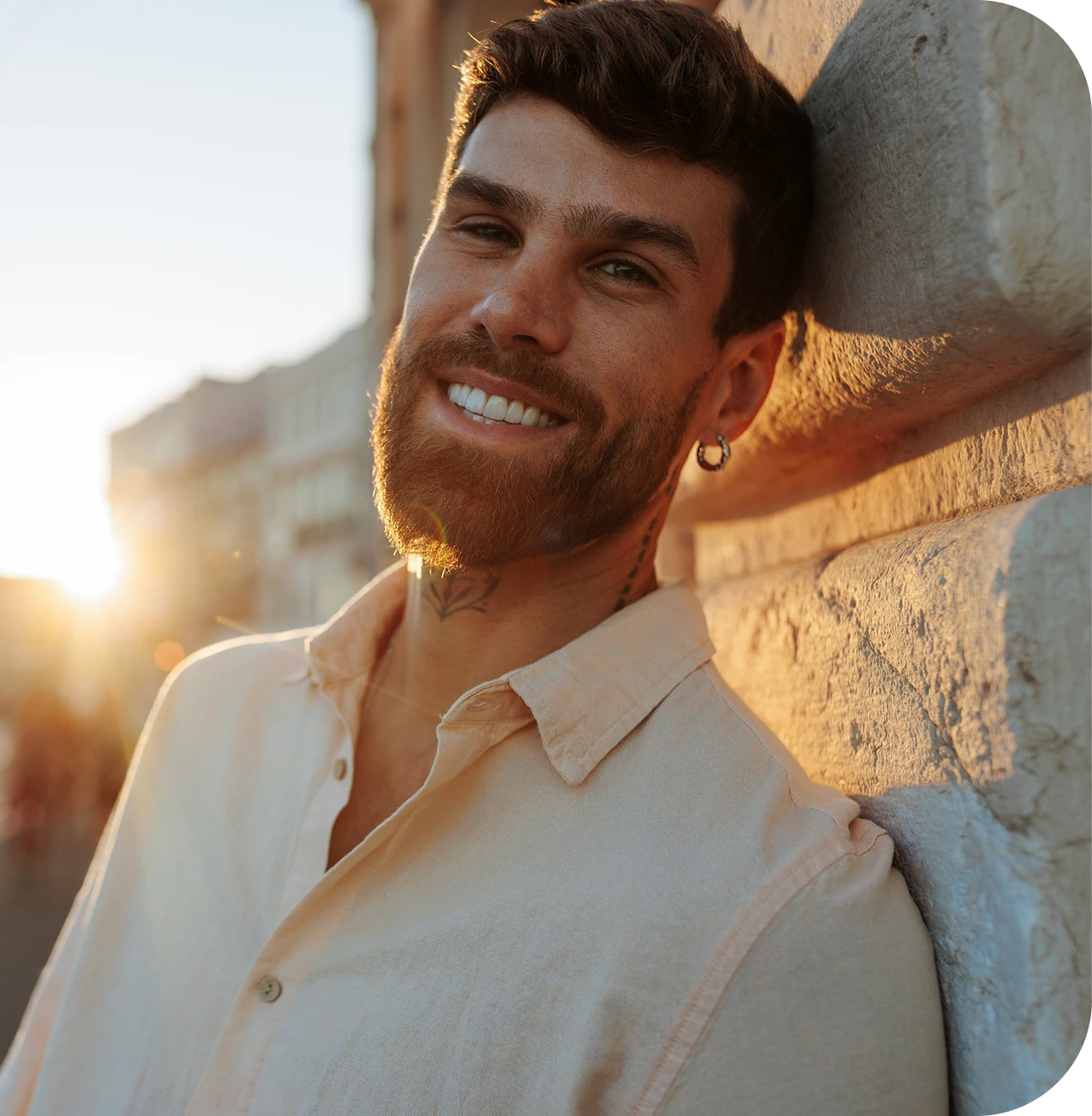 Man in light button-up shirt smiling at sunset against concrete wall