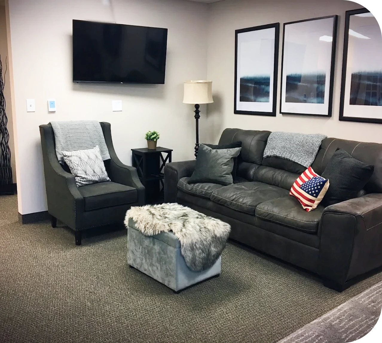 Therapy office lounge with black leather sofa, armchair, TV, lamp, and framed artwork