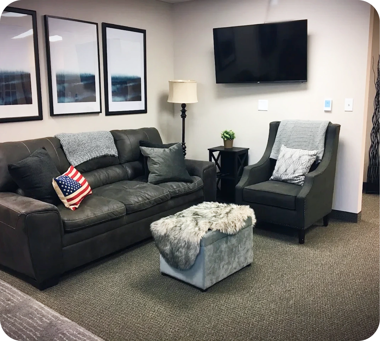 Modern therapy office waiting room with black leather sofa, accent chair, framed artwork, mounted TV, and decorative cushions