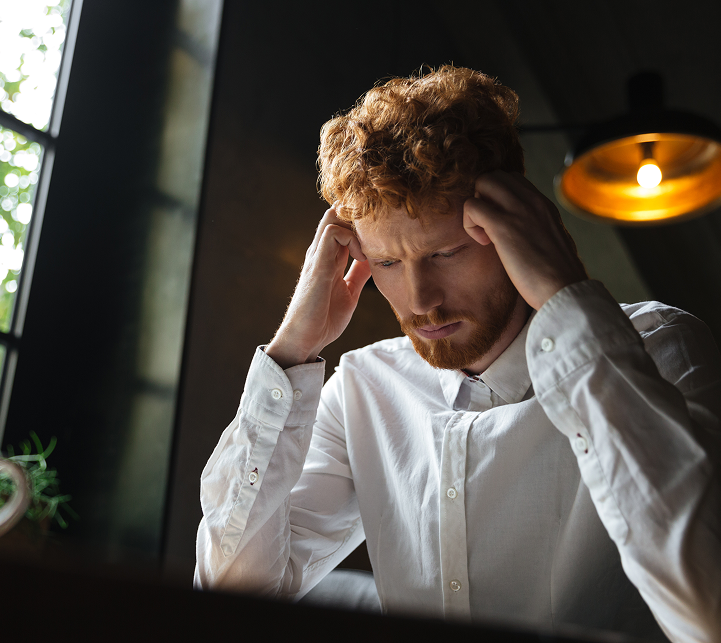 Man in white shirt with hands on head, eyes closed, expressing stress or discomfort