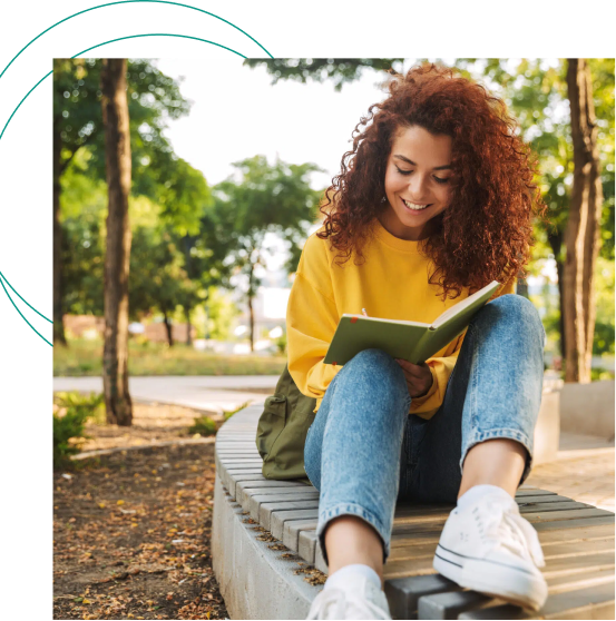 Woman in yellow shirt reading a book while sitting on a bench in a park