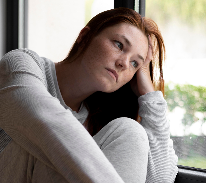Woman with reddish-brown hair looking troubled while sitting by a window