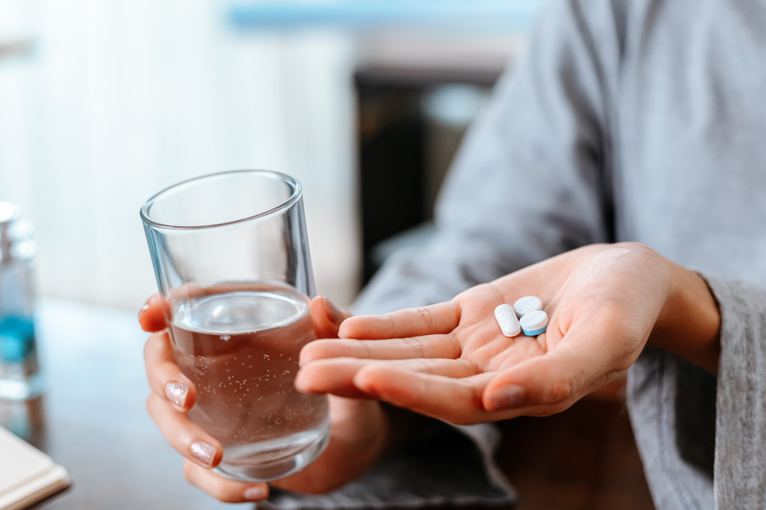 Person holding glass of water and white pills in palm of hand