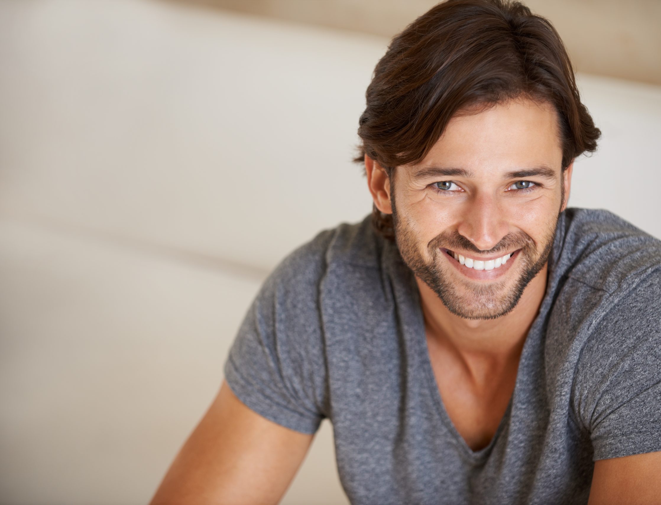 Man in gray t-shirt smiling at camera in bright indoor setting