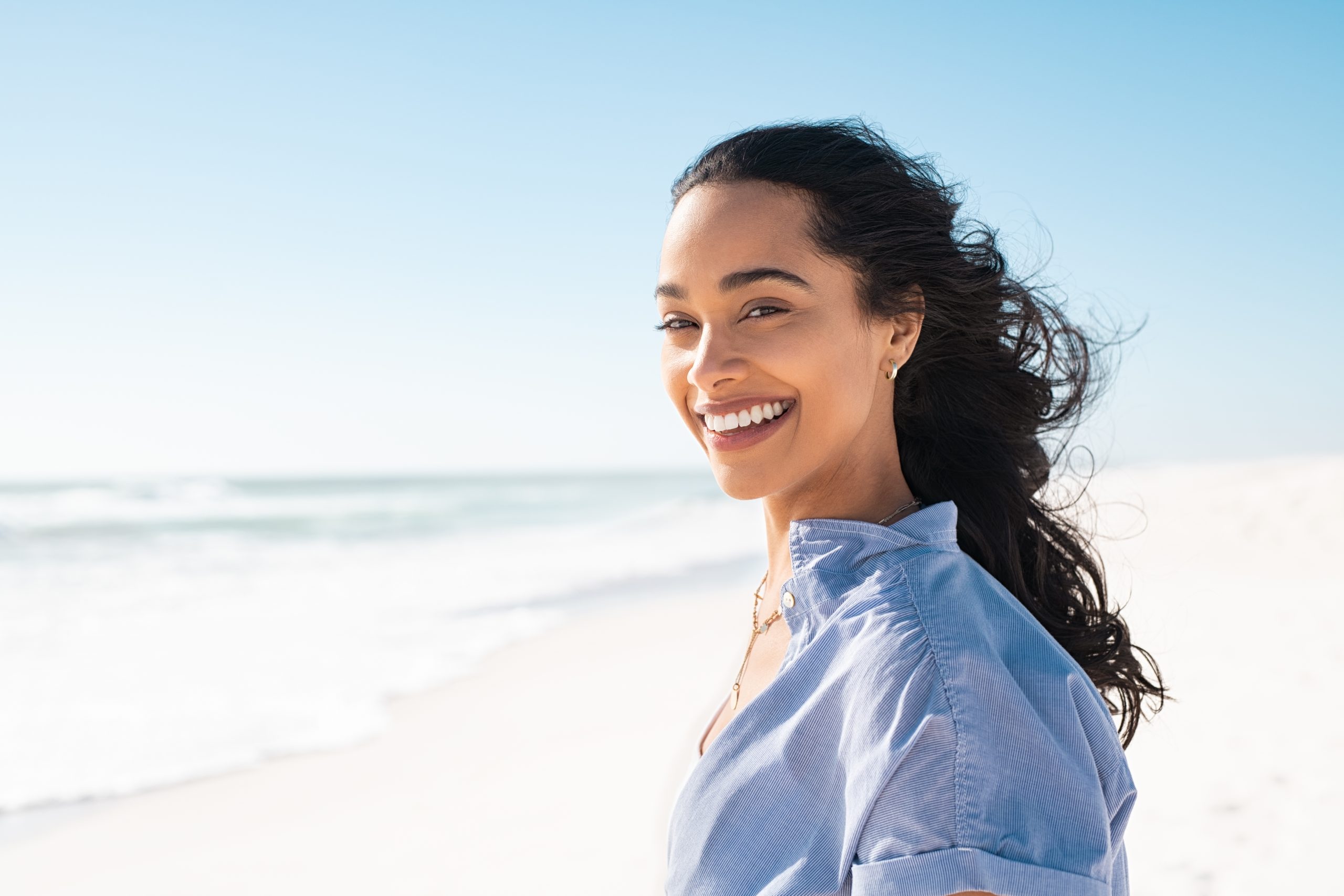 Woman laughing on beach with ocean behind her